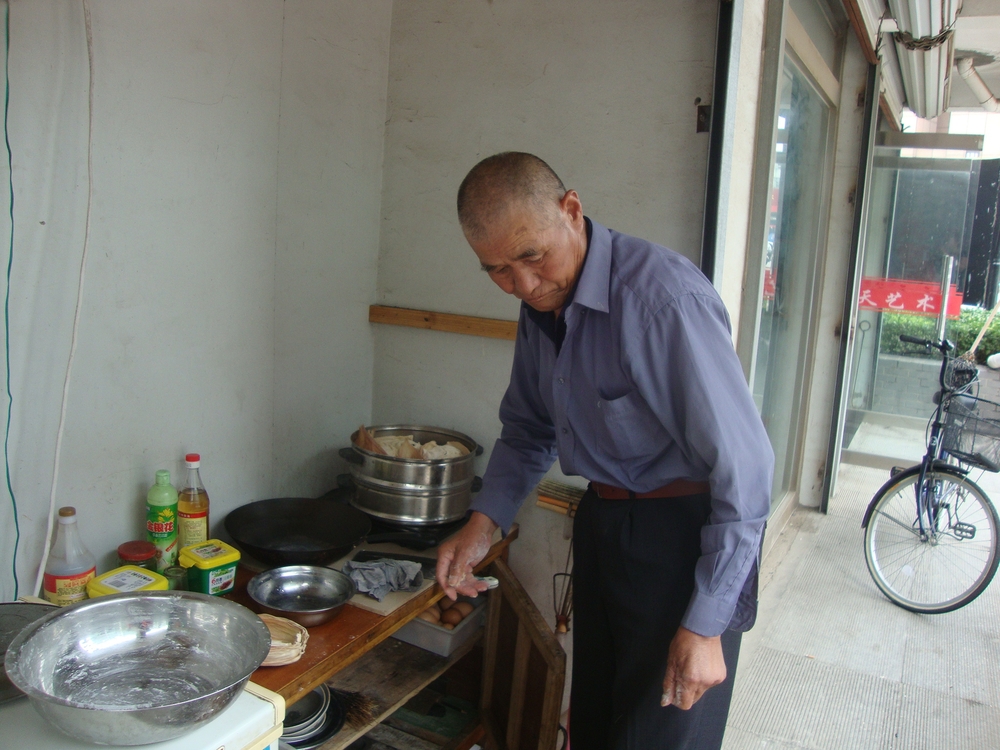 Китай, Пънлай, Мъж си готви пред магазина
